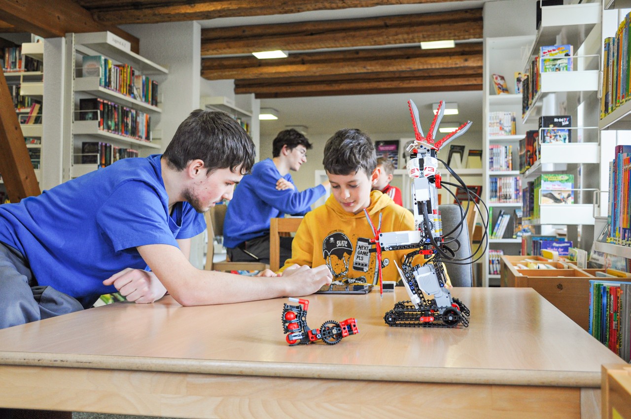 Ein junger Mann tüftelt mit einem Jungen an einem Roboter.