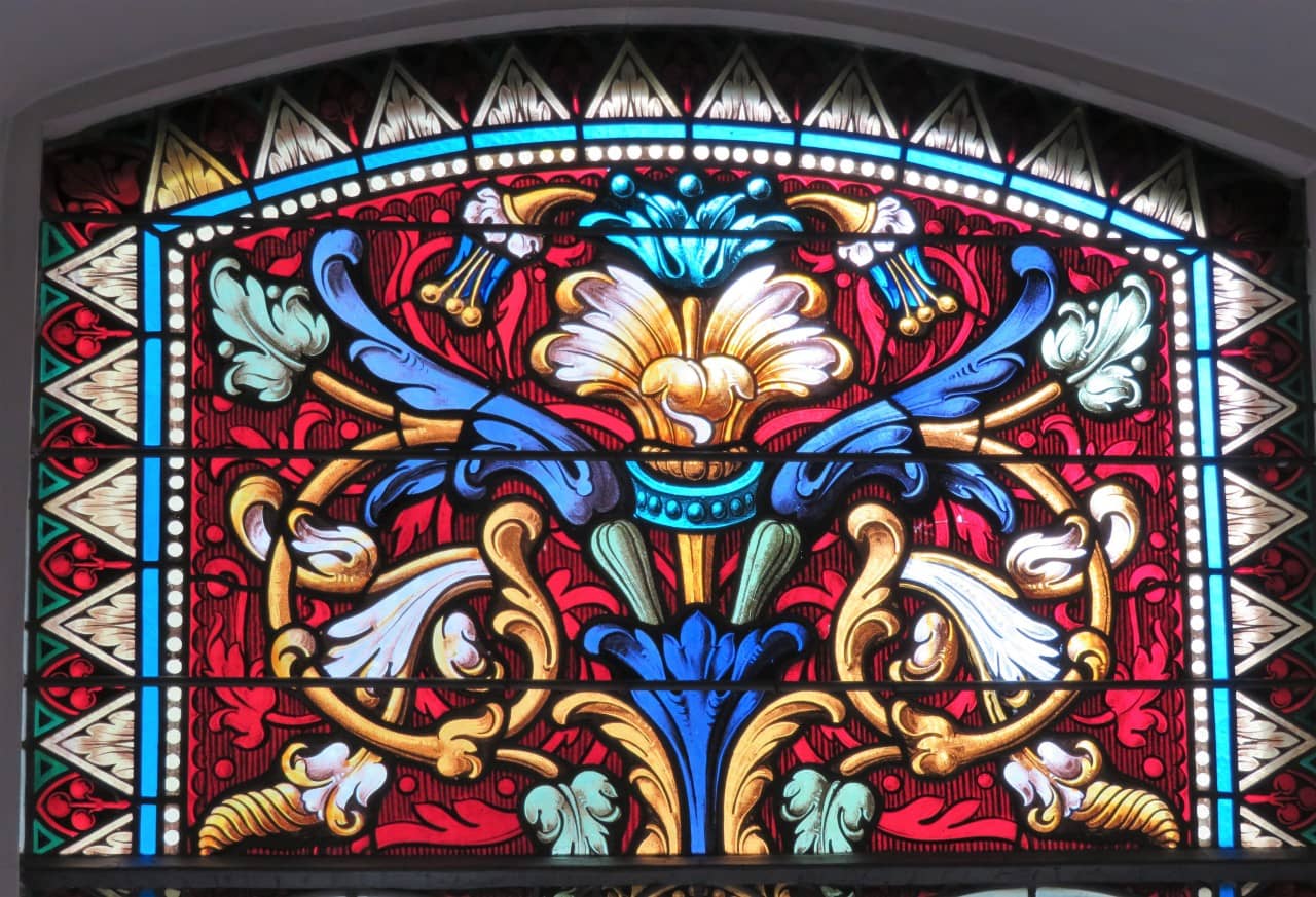 Symmetrische Pflanzenmotive bilden den oberen Abschluss der Glasmalerei in jedem der Fenster, die das Kirchenschiff zieren.