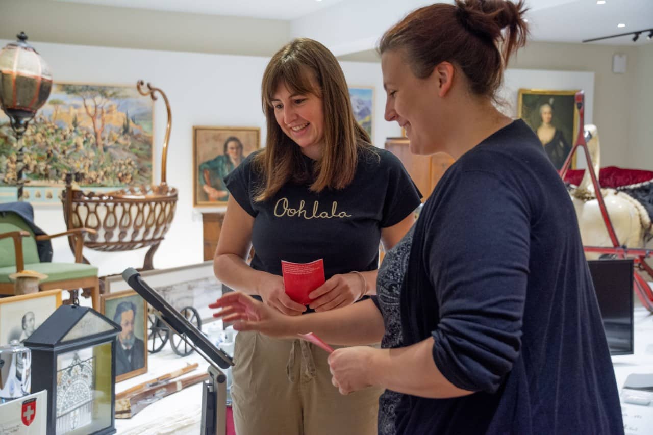 Zwei junge Frauen vor einem Tablet mit verschiedenen Museumsobjekten im Hintergrund