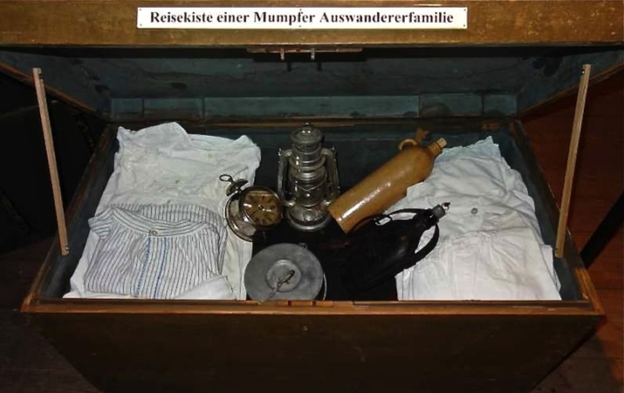 Geöffneter Koffer einer Auswandererfamilie mit sichtbarem Inhalt.