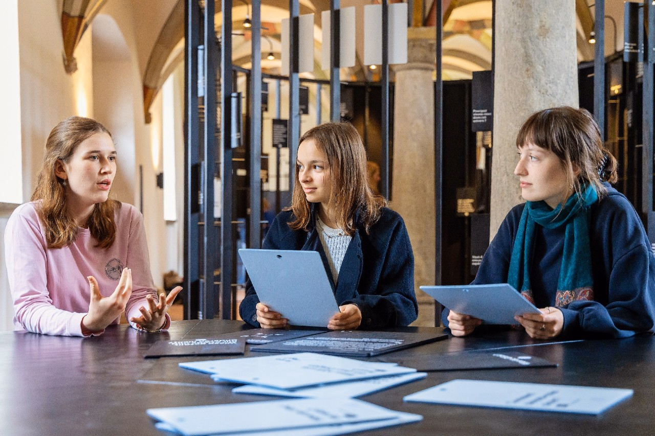 Drei junge Frauen sitzen in einem historischen Raum des Klosters Wettingen an einem Tisch und diskutieren miteinander.