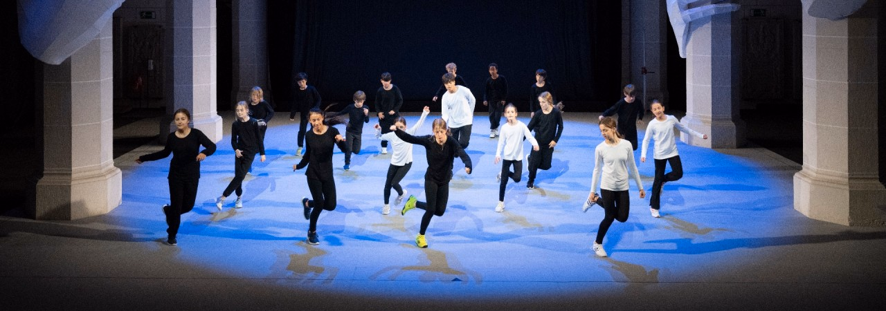 Weiss und schwarz gekleidete Gruppe von Schülerinnen und Schülern tanzen nebeneinander zwischen den Säulen der Klosterkirche Königsfelden.