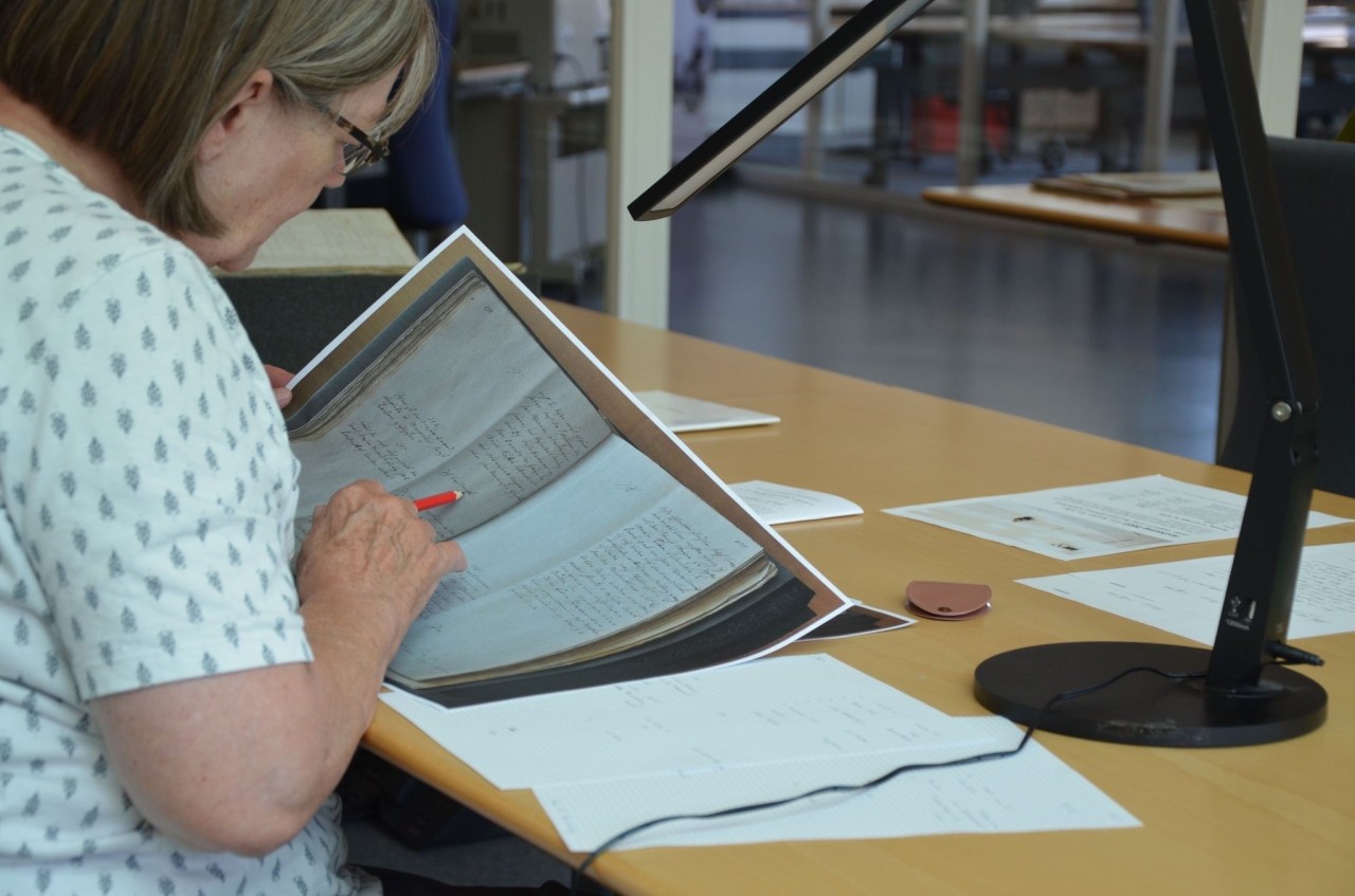 Frau sitzt an einem Tisch und liest in einem ausgedruckten Dokument mit einer alten Handschrift