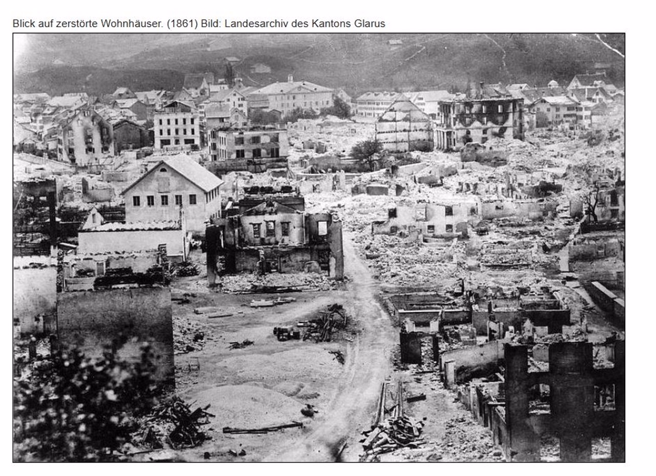 Zerstörte Wohnhäuser und Trümmerlandschaft in einer Stadt nach einem Brand.
