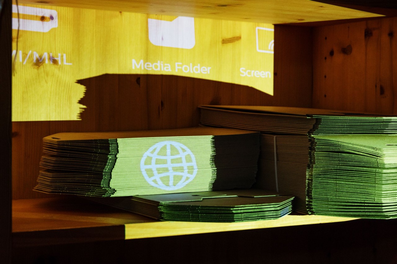Gestapelte Papierbögen in einem Holzregal, beleuchtet durch eine Projektion mit Symbolen, darunter eine Weltkugel.