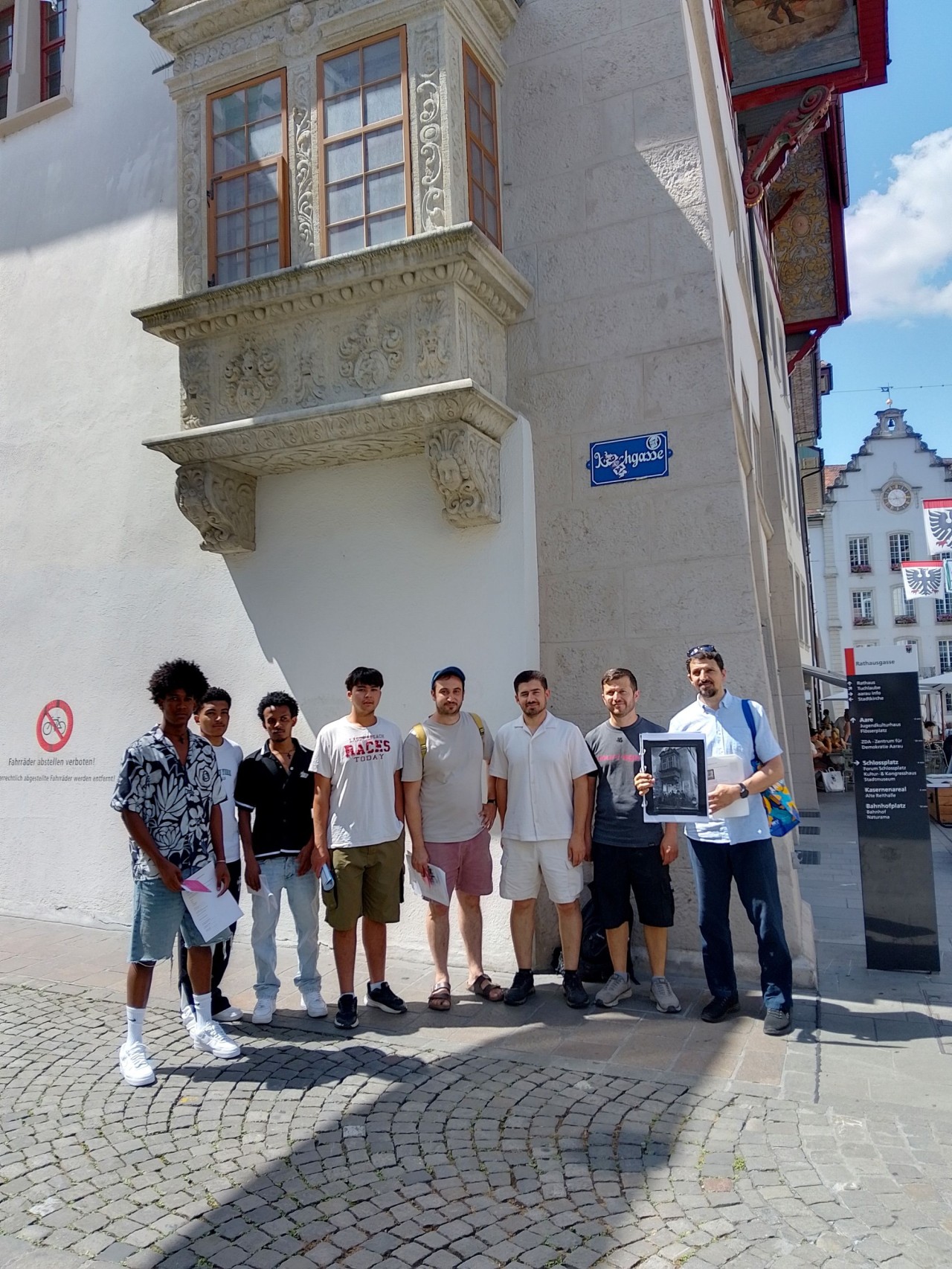 Eine Gruppe von acht Männern steht vor einem historischen Gebäude mit verziertem Erker und Strassenschild "Jungfraugasse".