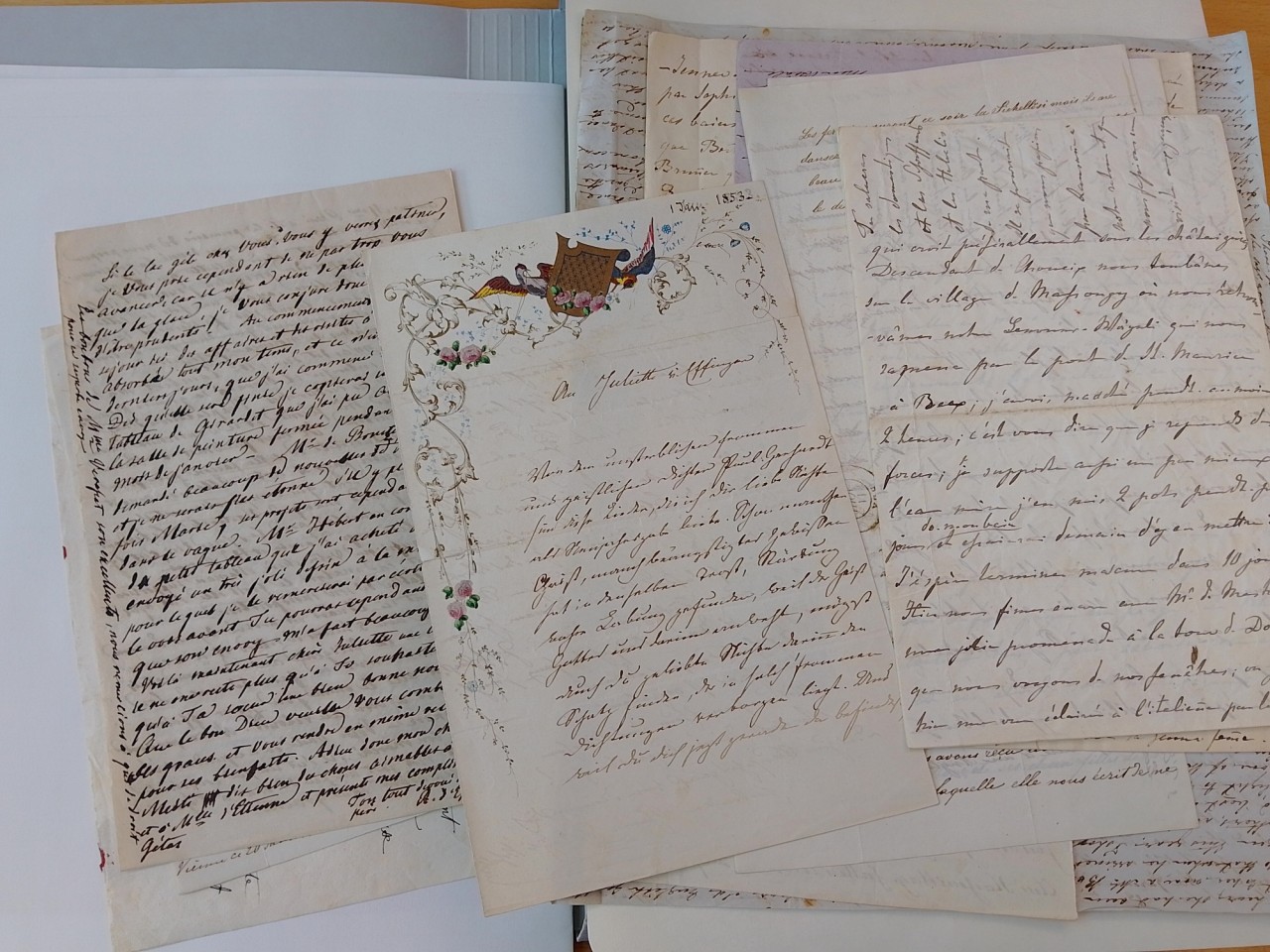 Mehrere alte handgeschriebene Dokumente auf einem Tisch liegend, teilweise mit Verzierungen und dichtem Text, teils in Dekorationsschrift.