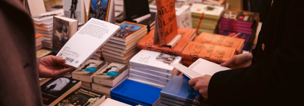 Personen stehen um einen reich gefüllten Büchertisch und blättern und lesen in Büchern.