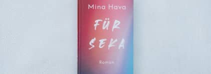 Das Buchcover mit dem mit einem dicken Marker handgeschriebenen Titel "Für Seka" besteht aus einem Farbverlauf in den Farbtönen pink, orange bis blau. Das Buch liegt auf einem weiss lackierten, krakelierten Untergrund.