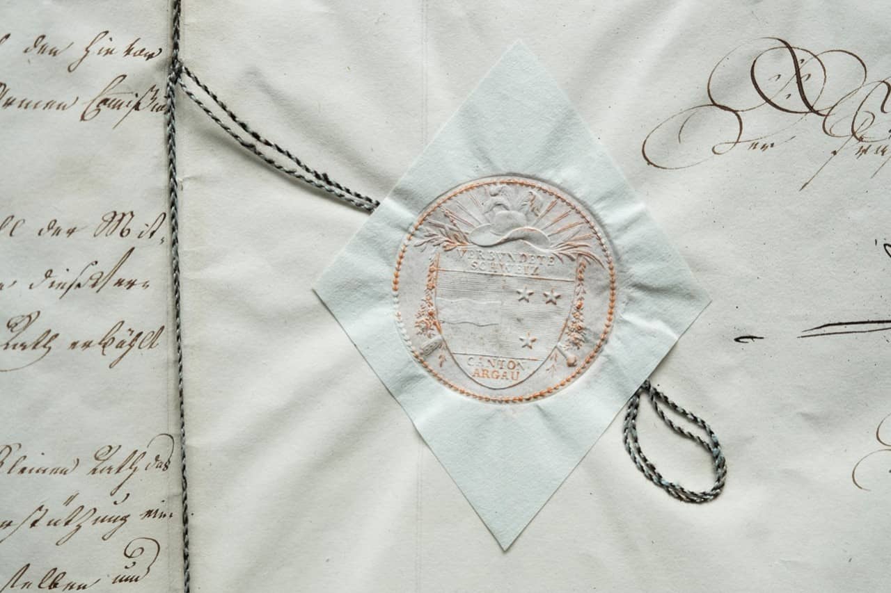 Das Bild zeigt ein Detail eines Siegels beziehungsweise eines Blindprägung eines Siegels aus dem Kanton Aargau. Das Detail schmückt das Armengesetz zum Schluss des Dokuments.