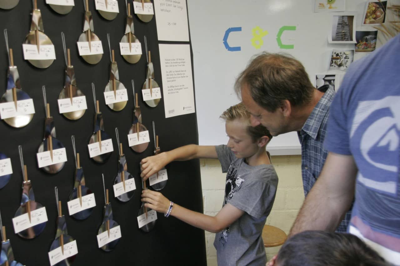 Schüler schaut mit Elternteil auf Installation mit Löffeln