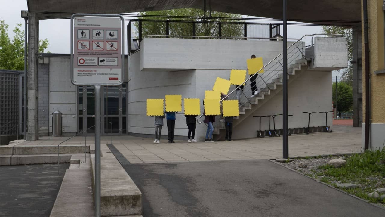 Schülerinnen und Schüler halten gelbe Vierecke vor ihre Gesichter