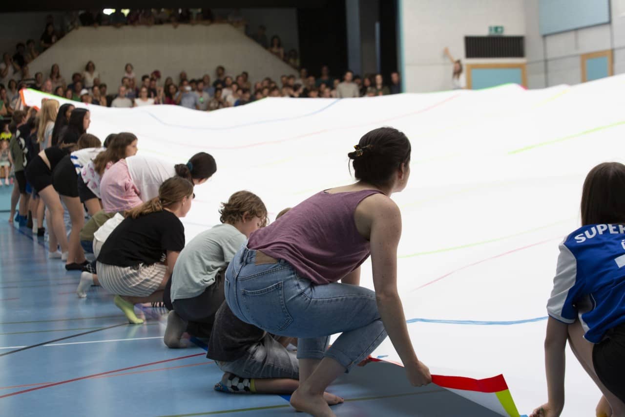 Schülerinen und Schüler sowie eine Lehrperson halten ein riesiges Papier in der Turnhalle