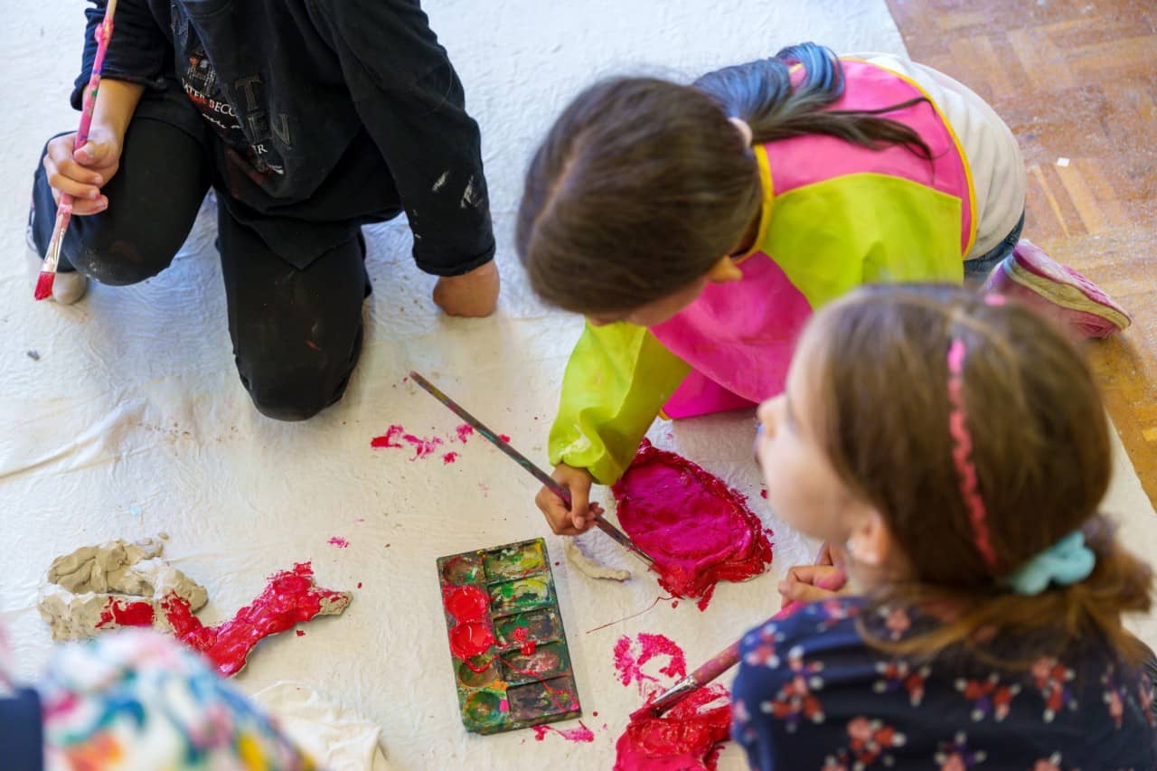 drei Schülerinnen und Schüler malen mit Pinseln am Boden