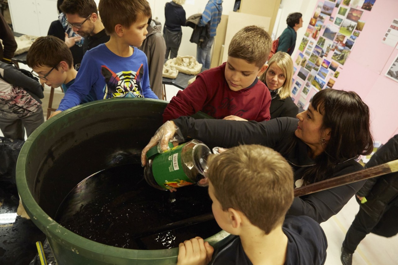 Künstlerin und Schüler leeren Flüssigkeit in ein grosses Becken