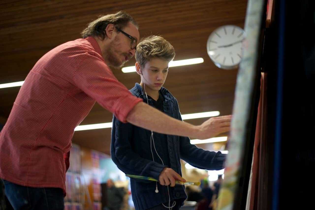Mann zeigt Schüler mit Kopfhörern ein Bild