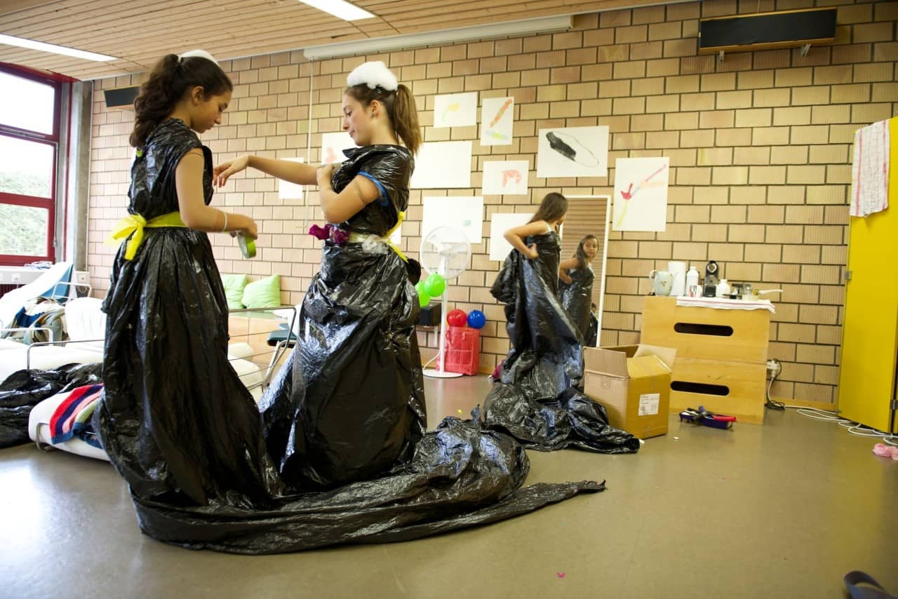 Schülerinnen tragen Kleider aus Plastik. Eine Schülerin steht vor dem Spiegel