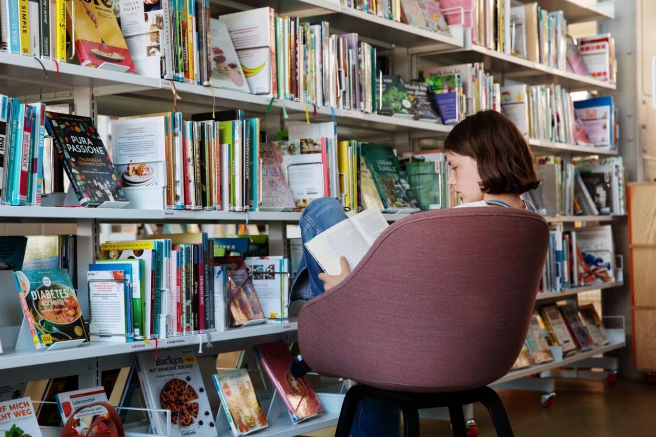 Schülerin sitzt auf einem Stuhl vor einem Bücherregal.