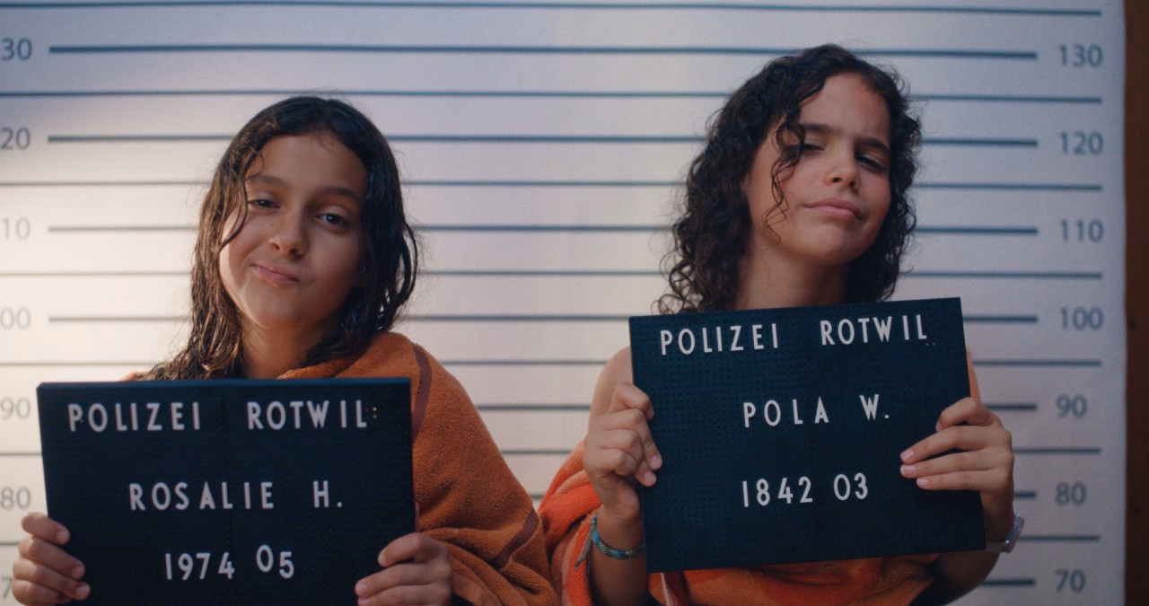 Zwei Mädchen stehen vor einer Wand und halten Schilder der Polizei in die Höhe.