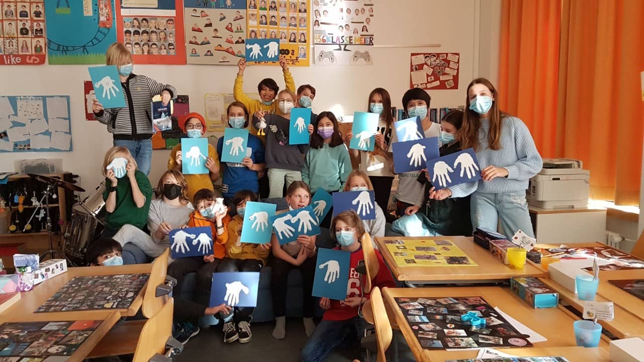 Ein Gruppenfoto von Schülerinnen und Schülern. Alle halten ein blaues Blatt mit einer weissen Hand darauf hoch.