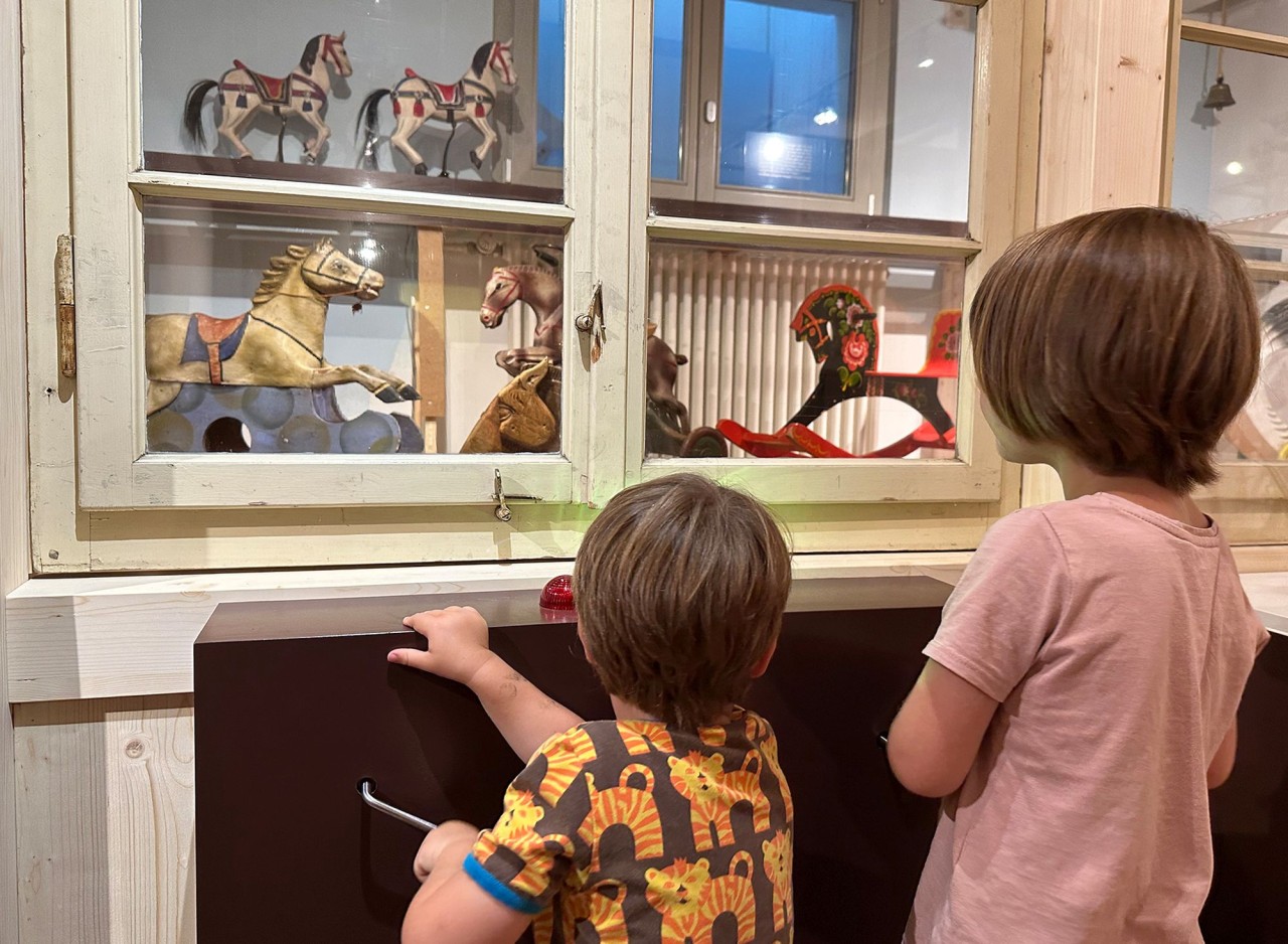 Zwei Schülerinnen und Schüler schauen Pferdefiguren an, die in einer Vitrine stehen. 