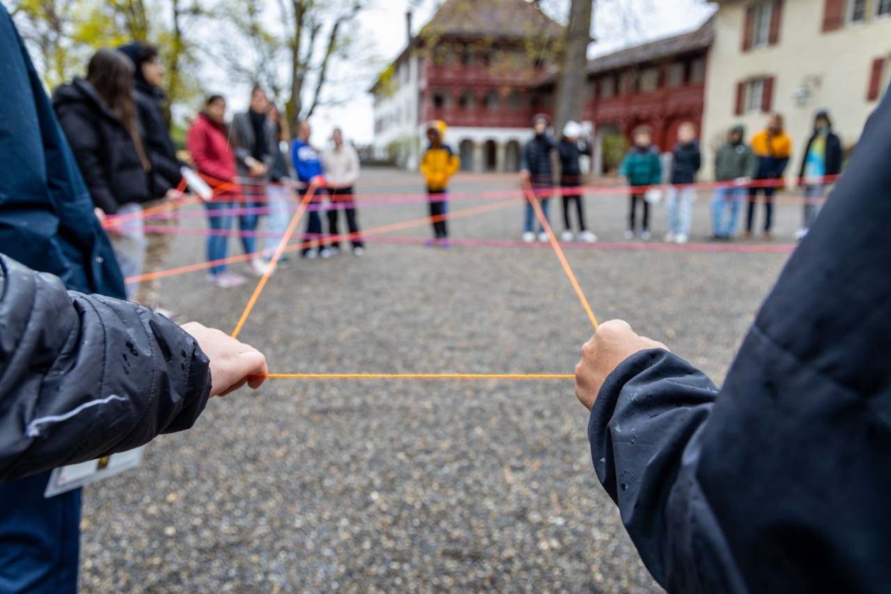 Schülerinnen und Schüler stehen in einem grossen Kreis und spannen mit ihren Händen eine Schnur.