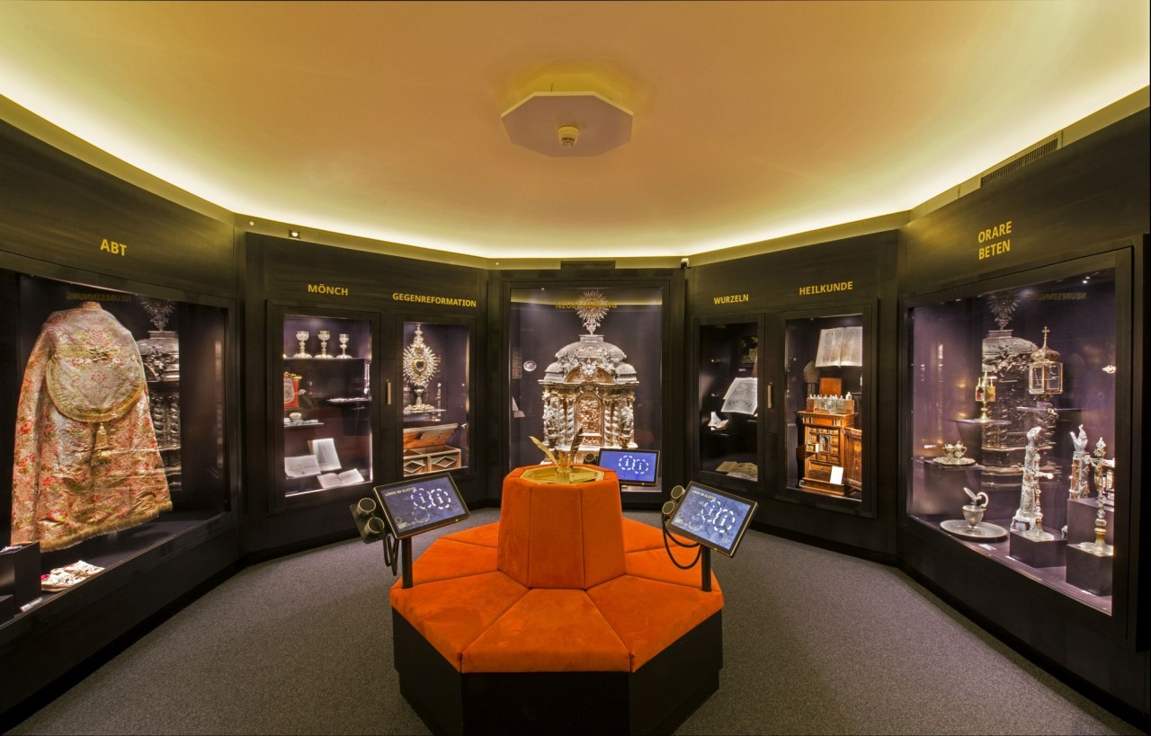 Eine Aufnahme des Ausstellungsraums zeigt prunkvolle sakrale Gegenstände in Vitrinen. 