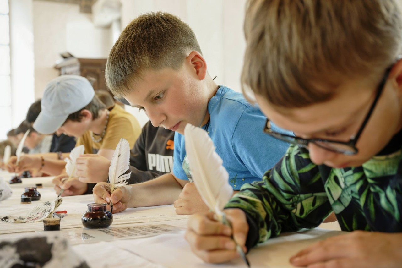 Kinder beim Schreiben mit Federn auf Papier.
