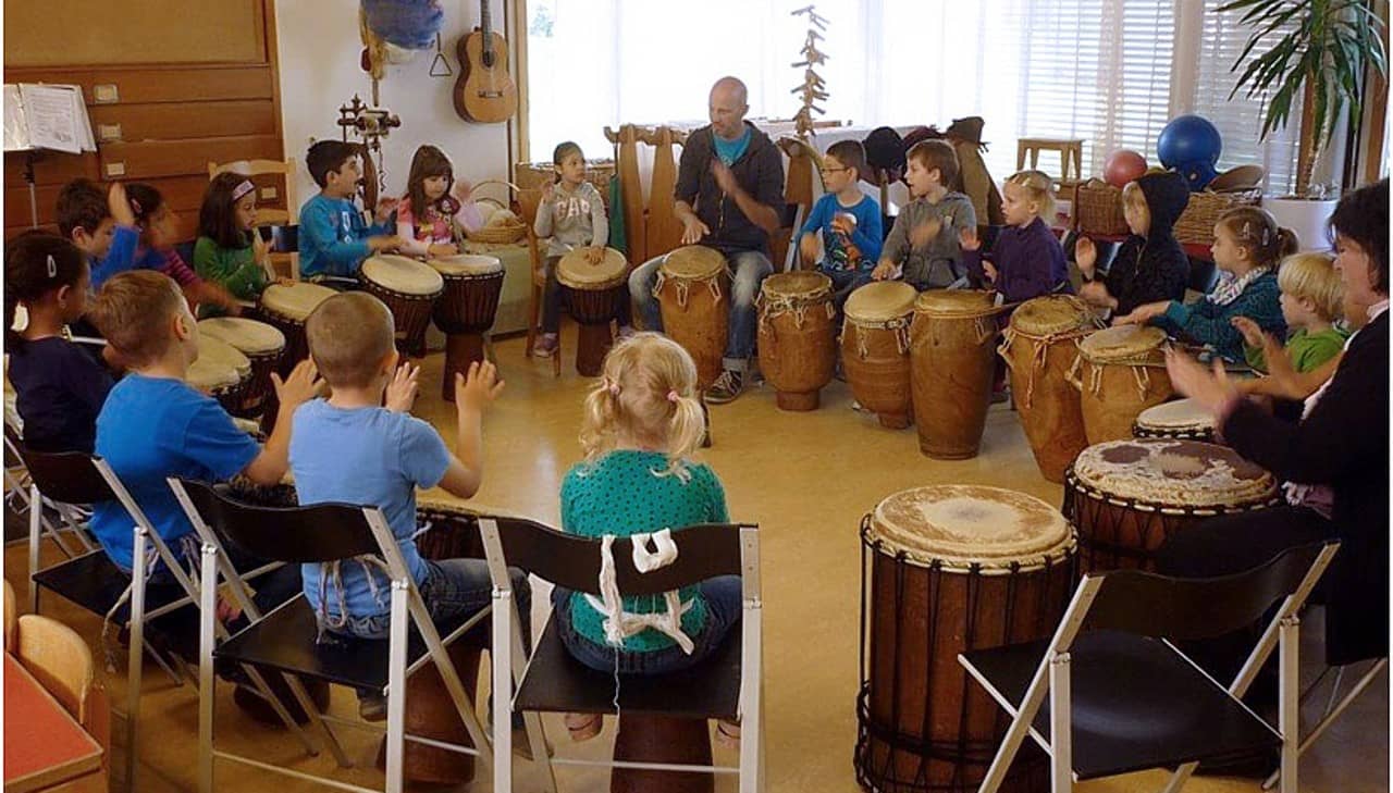 Schülerinnen und Schüler mit Trommeln sitzen in einem Kreis.