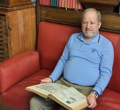Bruno Altherr sitzt auf einem roten Sofa und präsentiert ein altes Buch.