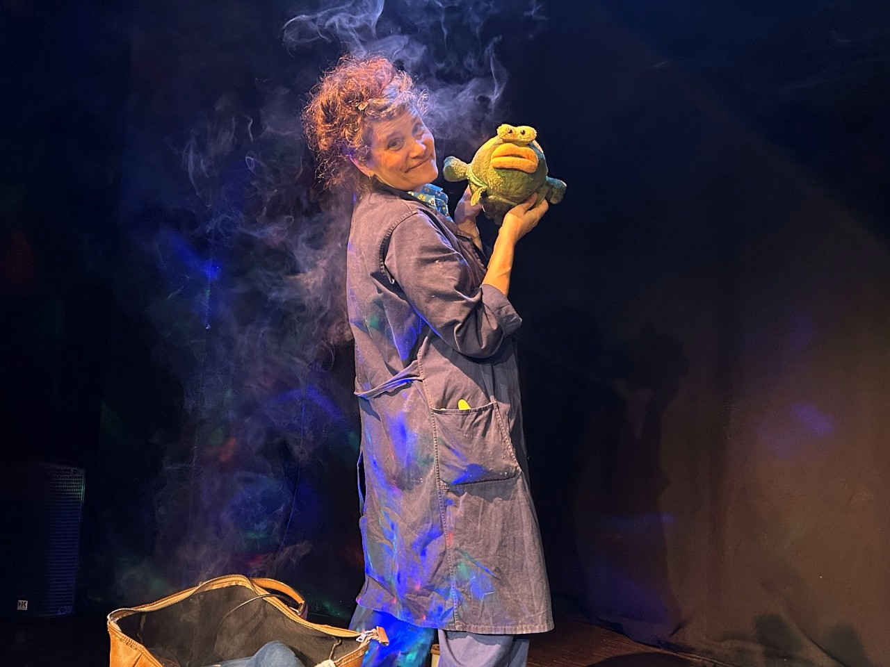 Eine Frau steht auf einer Bühne und hält einen Frosch aus Plüsch in der Hand.