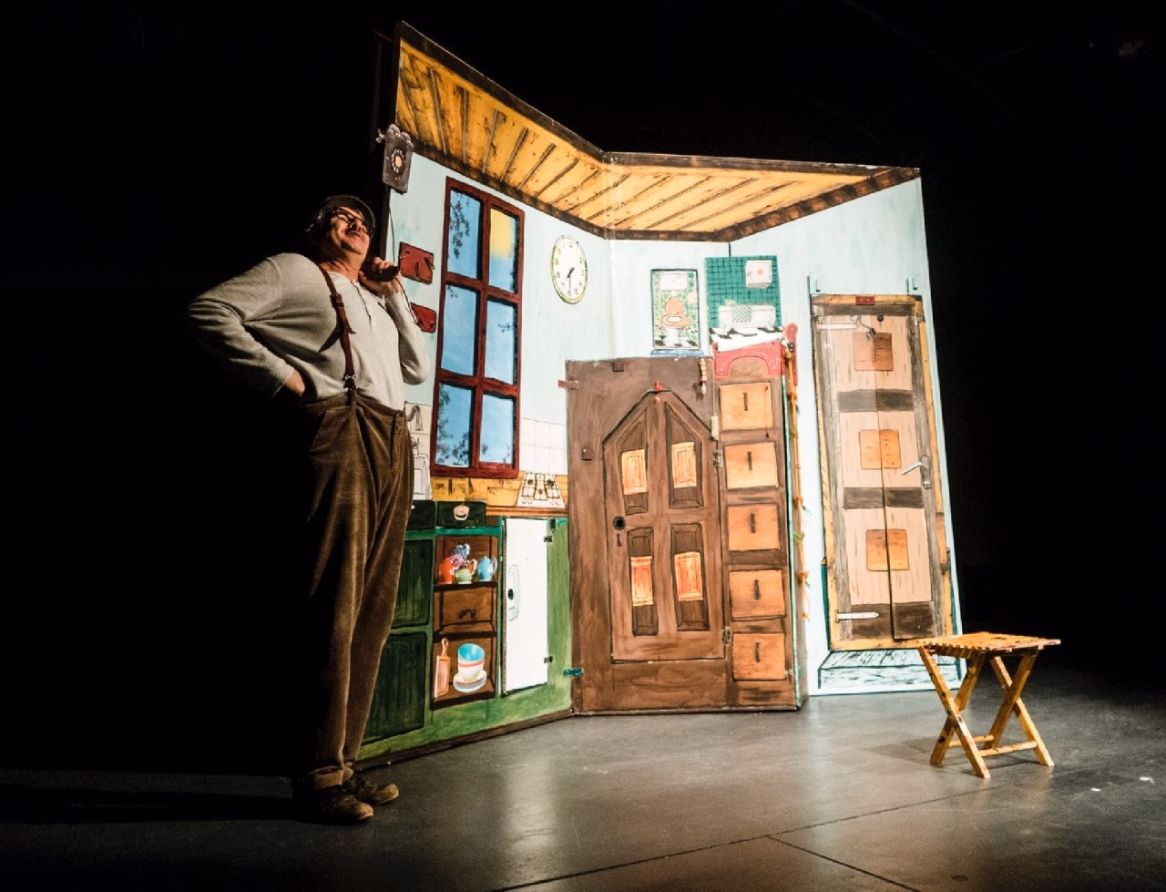 Ein Mann steht auf einer Bühne. Im Hintergrund befindet sich das Bühnenbild - ein Zimmer.
