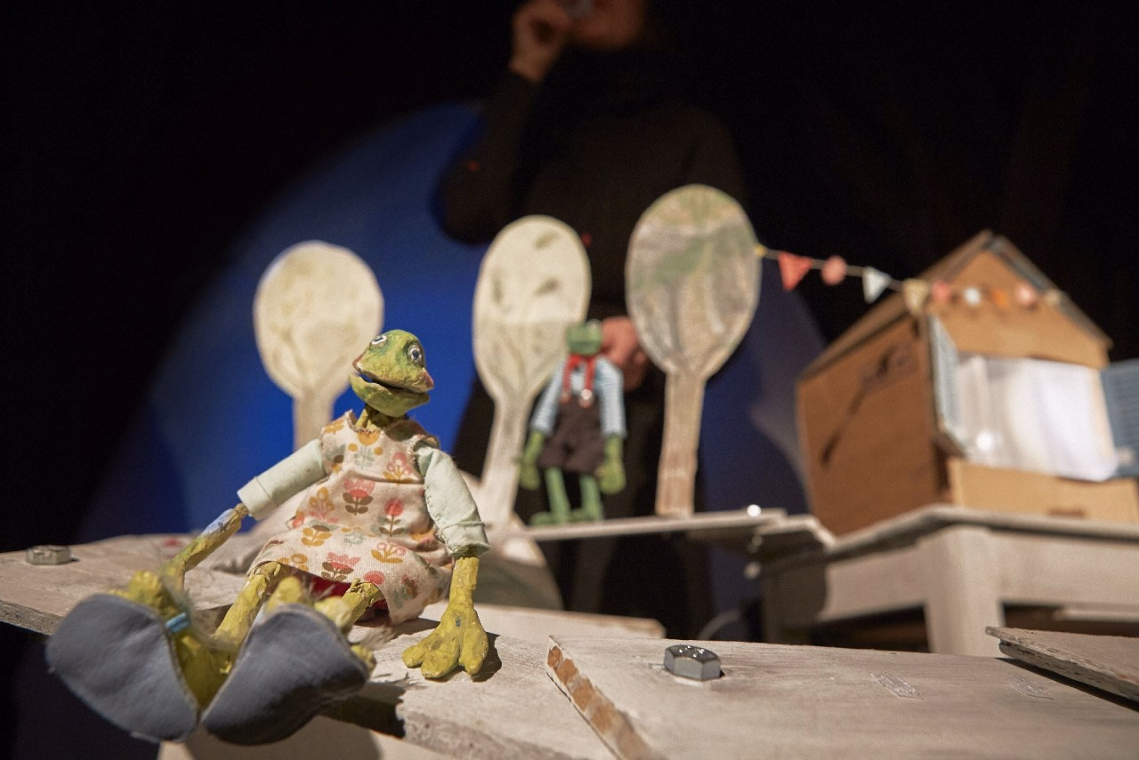 Eine Echsenfigur sitzt vor einem Haus.