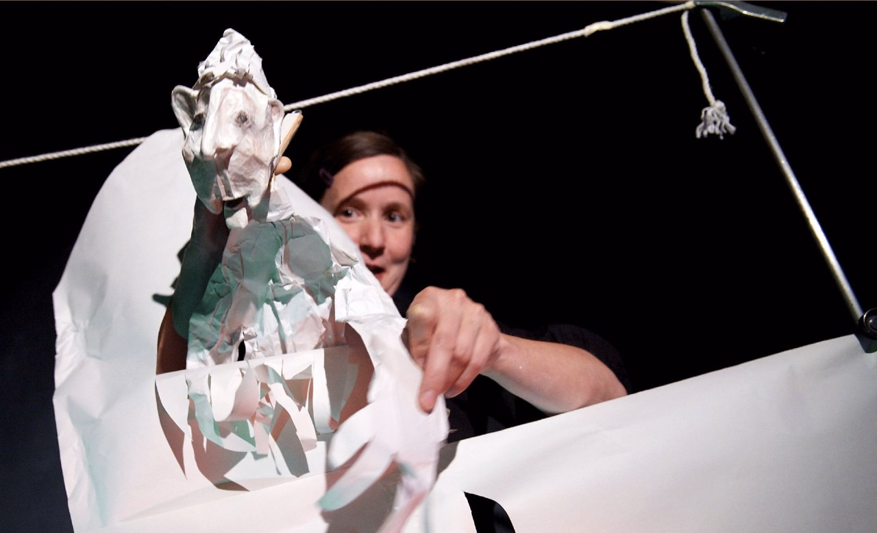 Eine Figurenspielerin hält eine menschliche Figur, die ganz weiss ist.