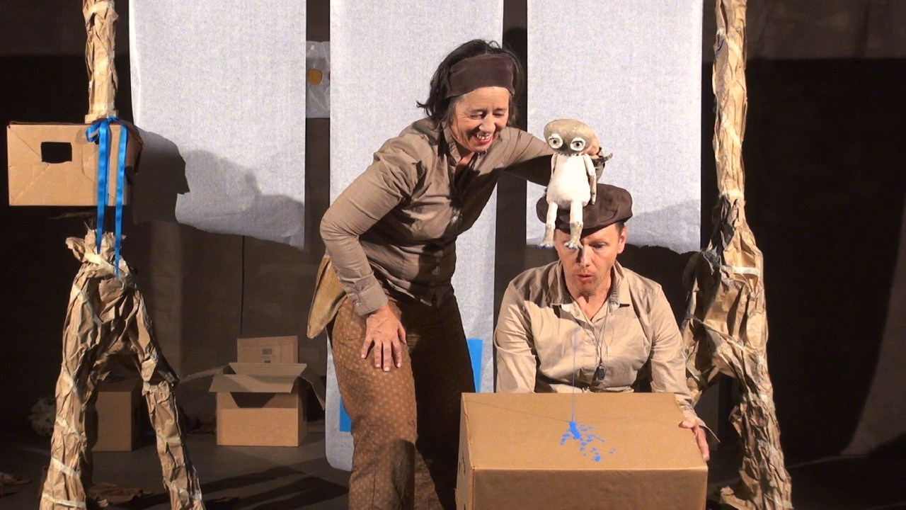 Eine Frau und ein Mann sind uaf der Bühne. Sie befinden sich in einem Wald. Die Frau hält eine Eule.