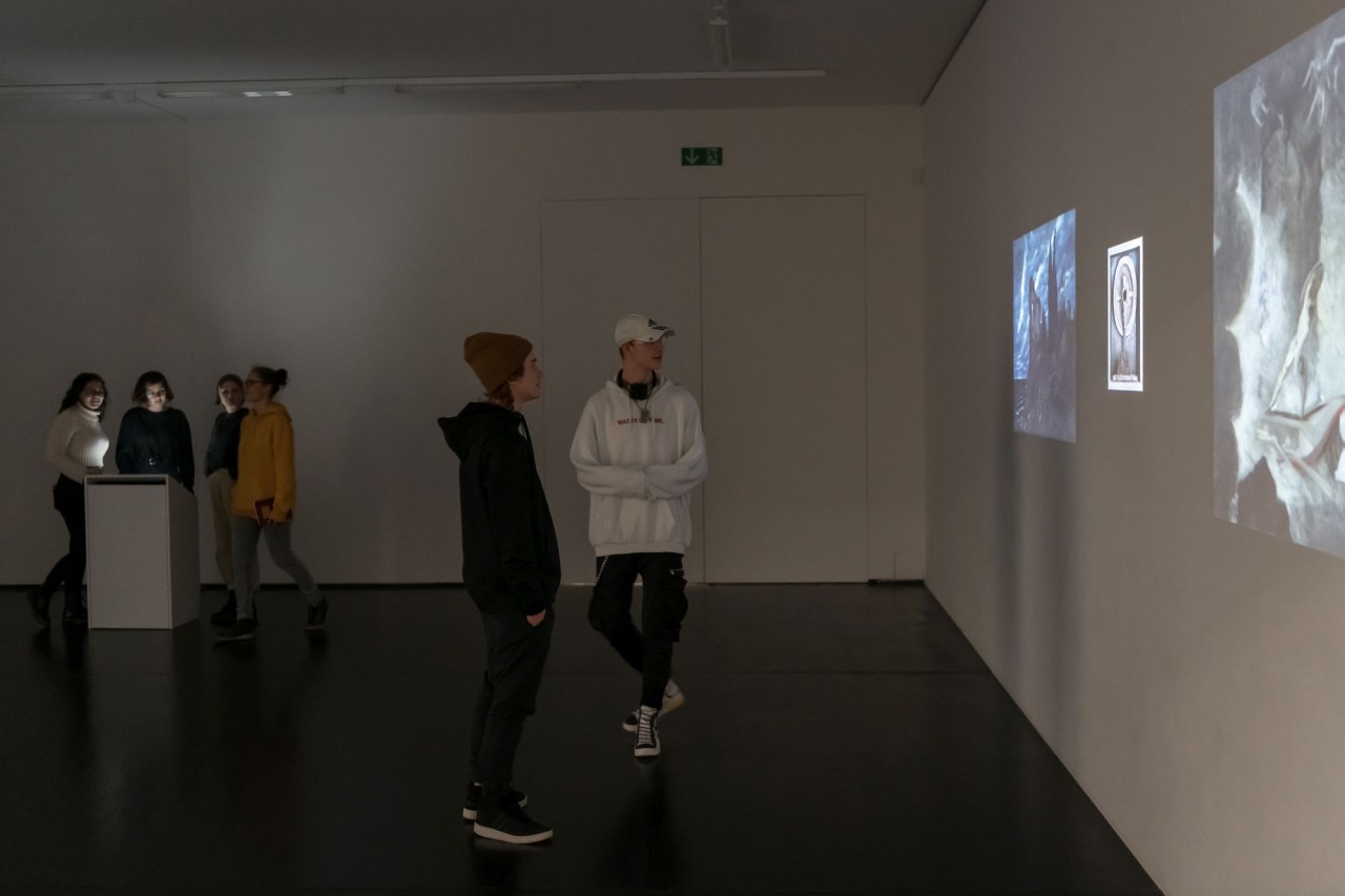Schülerinnen und Schüler in einem Ausstellungsraum. Es werden Kunstwerke an die Wand projiziert.