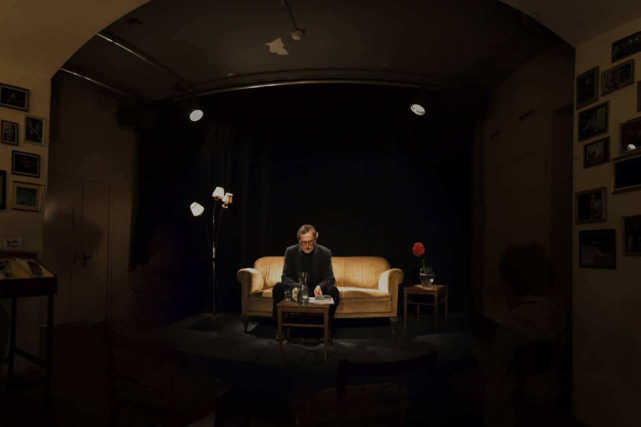 Klaus Merz sitzt auf einem Sofa in dunklem Licht