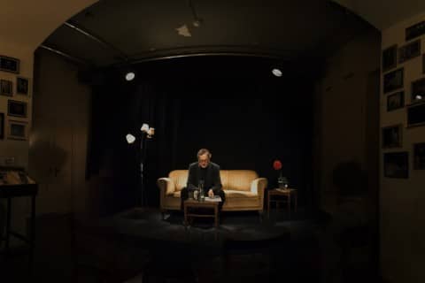 Klaus Merz sitzt auf einem Sofa in dunklem Licht