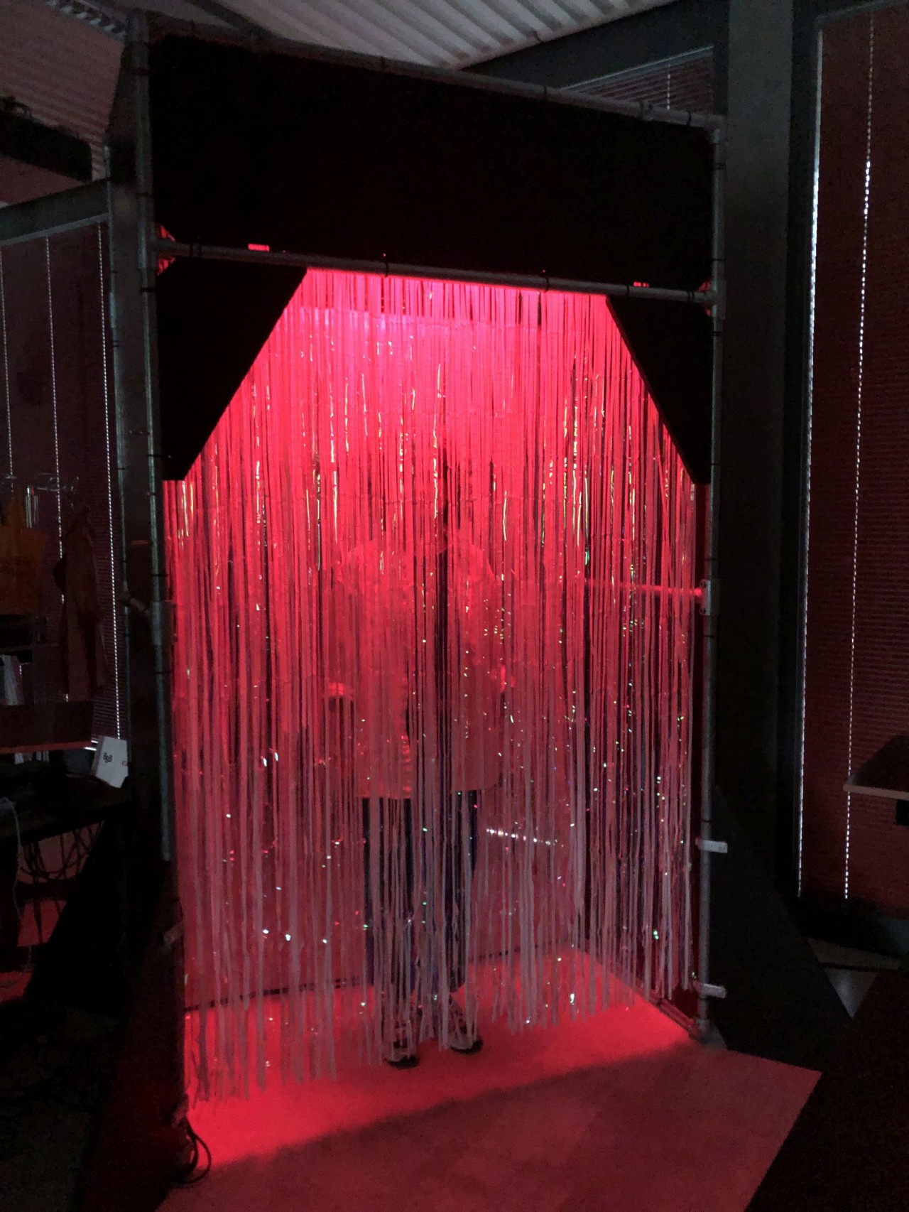 Die Darstellung zeigt das "Sound Gate". Person steht hinter schimmernden, durchsichtigen Fäden in einer dunklen Umgebung, beleuchtet durch rotes Licht.