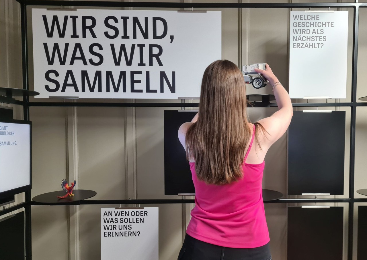 Junge Frau mit Kamera vor Plakaten.