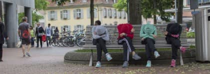 Kinder und Jugendliche sitzen bei einem öffentlichen Platz und haben ihre Köpfe in ihre verschränkten Arme gelegt