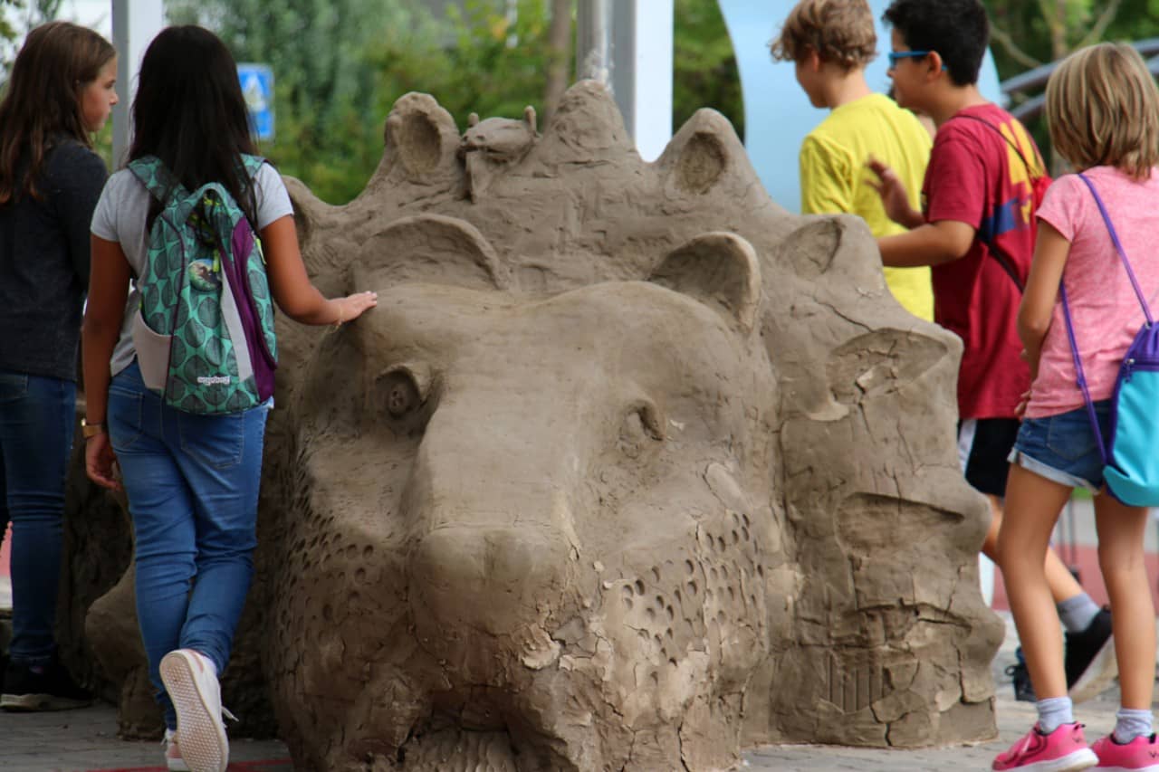Kinder bauen an ihrer überlebensgrossen Löwenskulptur aus Lehm