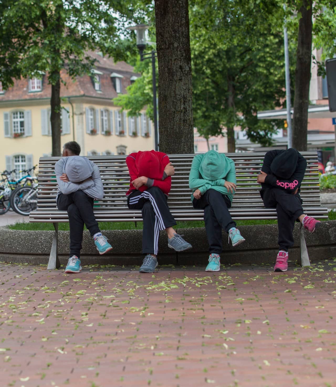 Vier Jugendliche sitzen mit gesenkten Köpfen nebeneinander auf einer Parkbank.