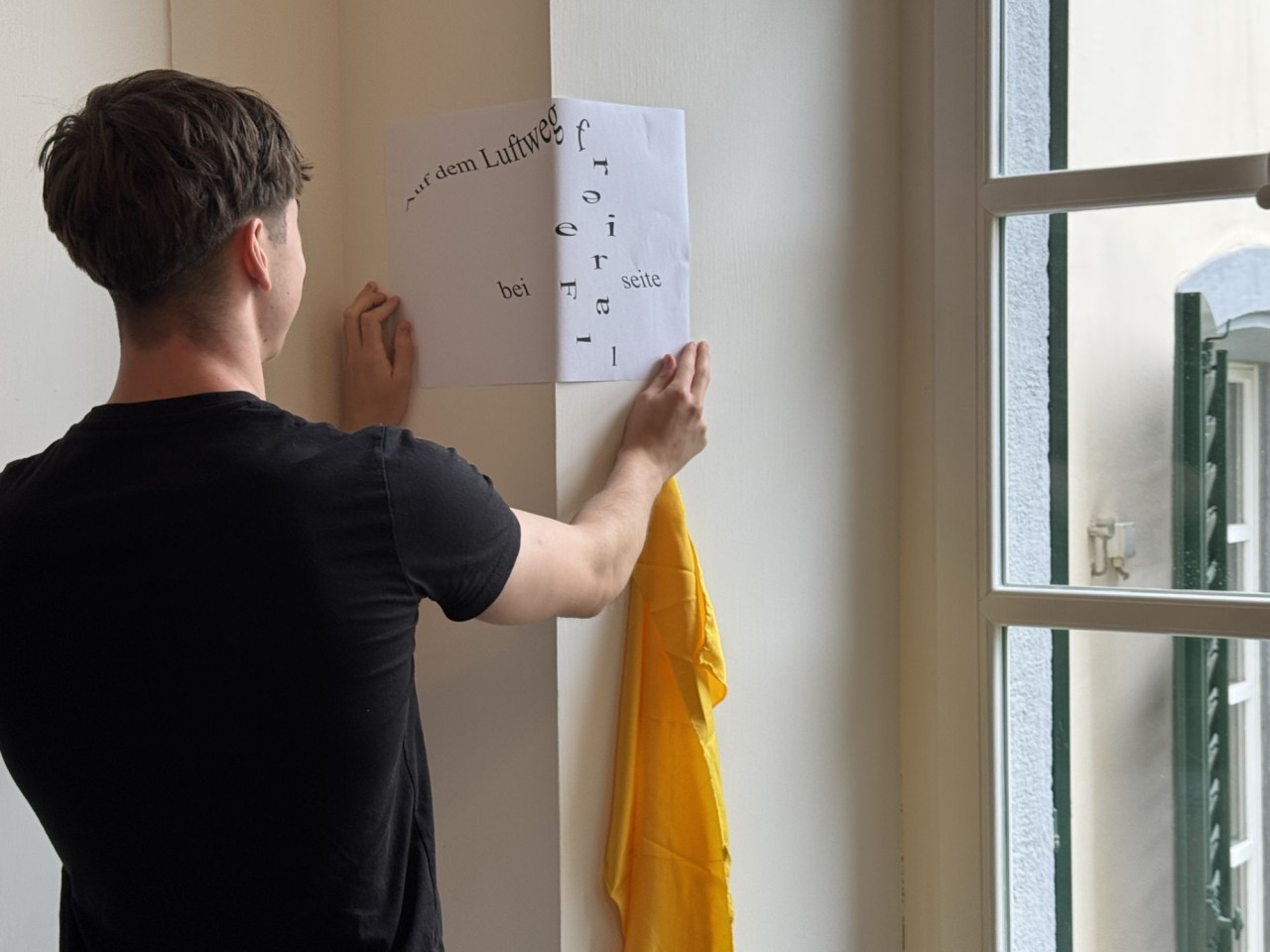 Ein junger Mann hält ein Blatt Papier mit einem Text darauf an eine Wand.