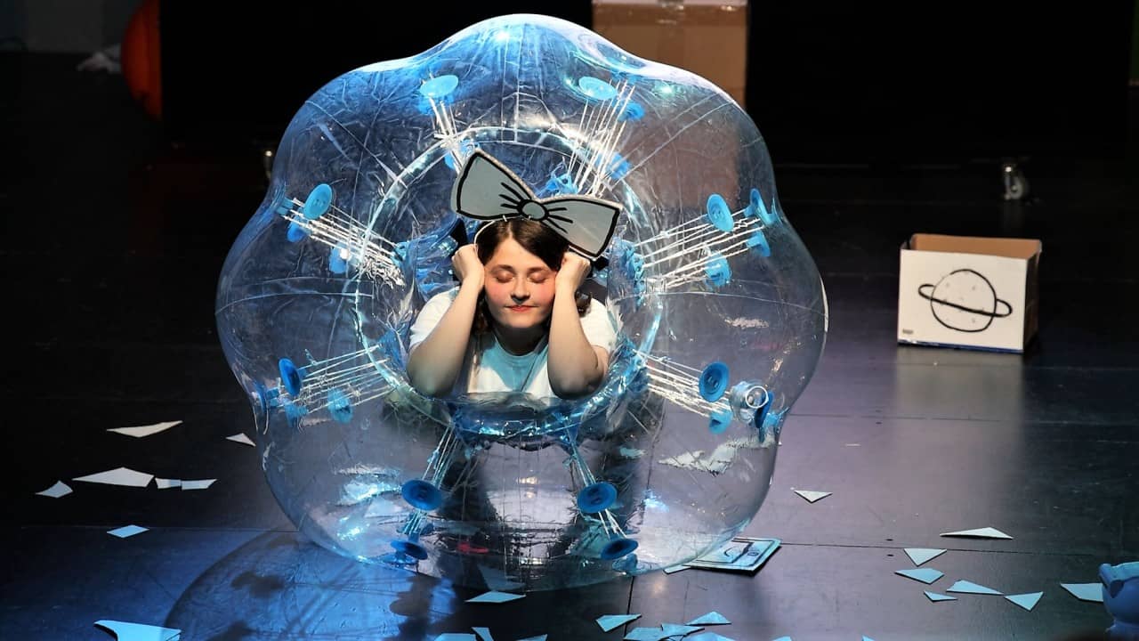 Eine verkleidete junge Frau mit geschlossenen Augen steckt in einem grossen Plastikball.