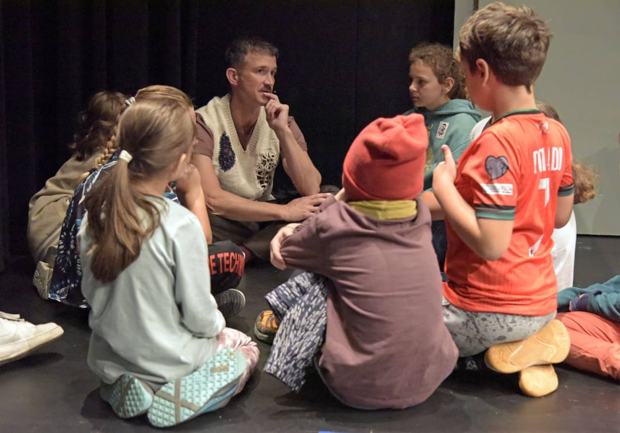 Ein Erwachsener und sieben Kinder sitzen im Kreis und reden miteinander