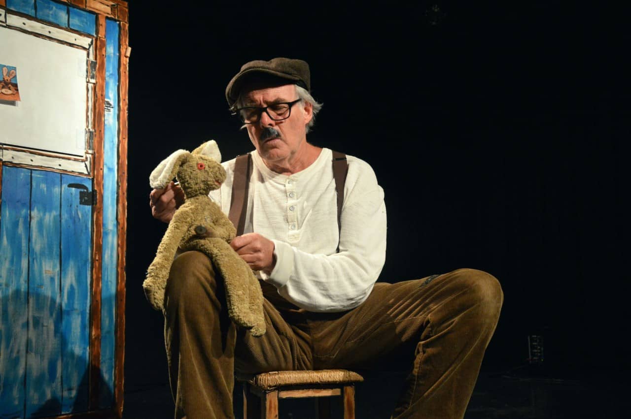 Man sitzt auf Hocker und spricht mit einer Hasenpuppe