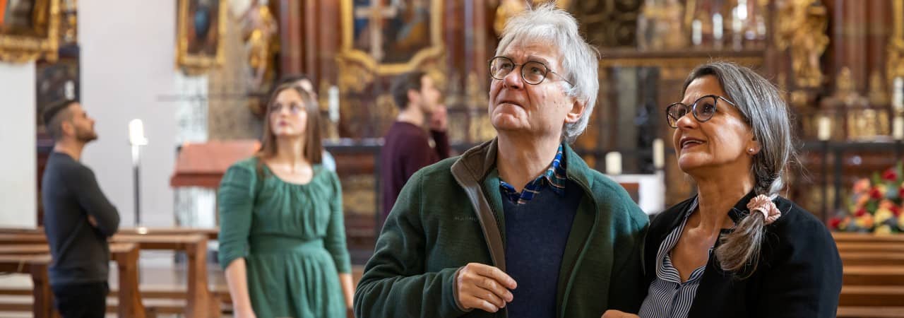 Ein Ehepaar steht in der Klosterkirche, sie blicken nach oben. Im Hintergrund stehen weitere Personen