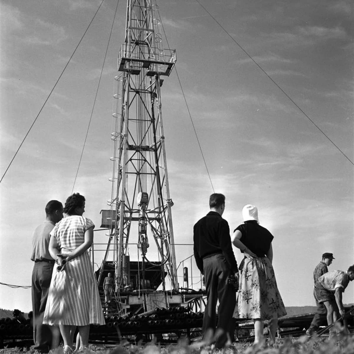 Eine Gruppe von Männern und Frauen sieht bei einer Erdölbohrung zu. 