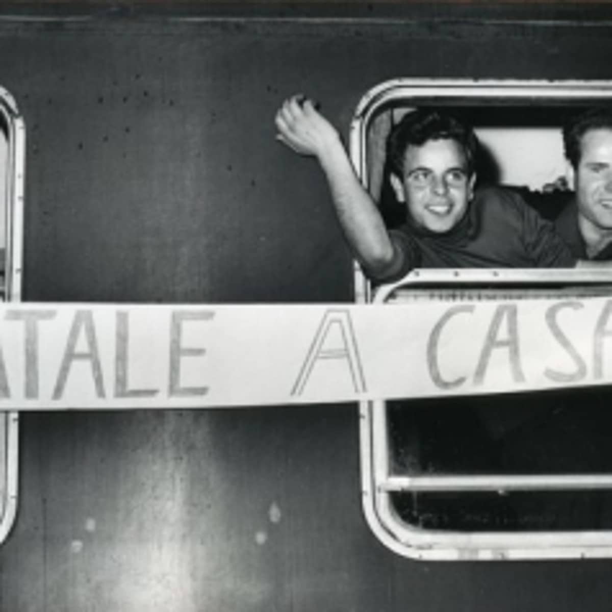 Italienische Gastarbeiter halten ein Transparent mit der Aufschrift „Natale a casa“ aus einem Zugfenster.